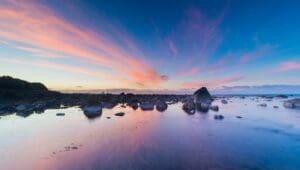 A body of water with rocks and some clouds in the sky