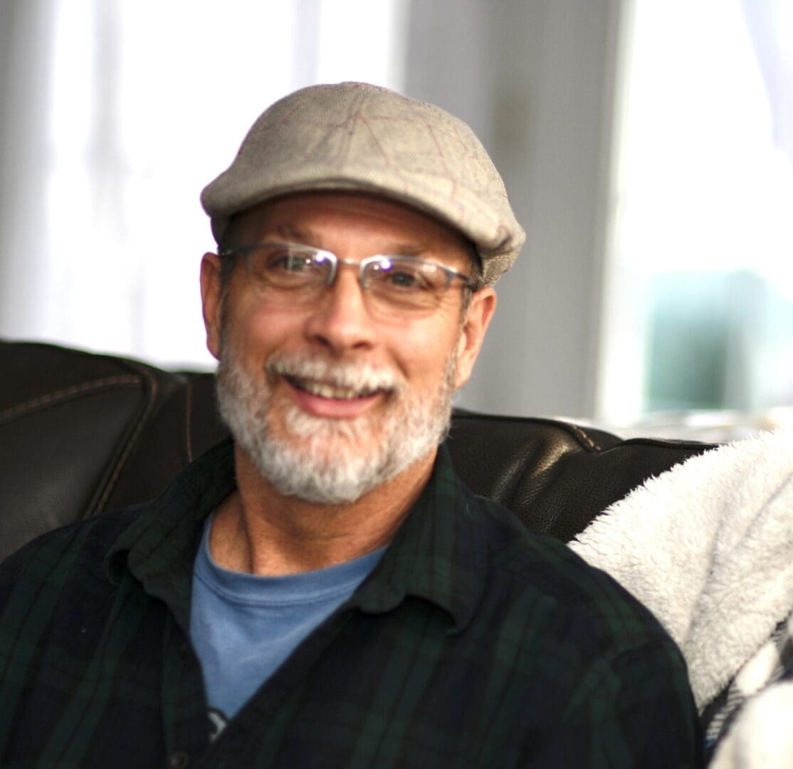 A man with glasses and a hat sitting on the couch